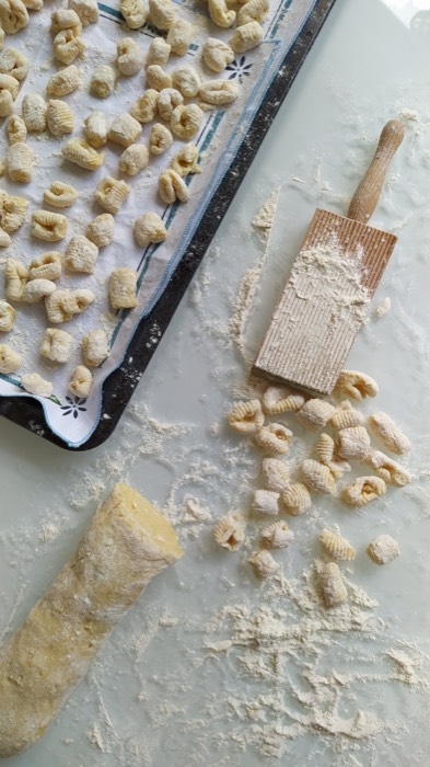 Gnocchi on a tray next to a block of Parmigiano and a grater