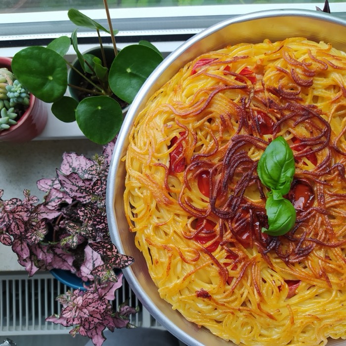 A golden spaghetti pie topped with basil